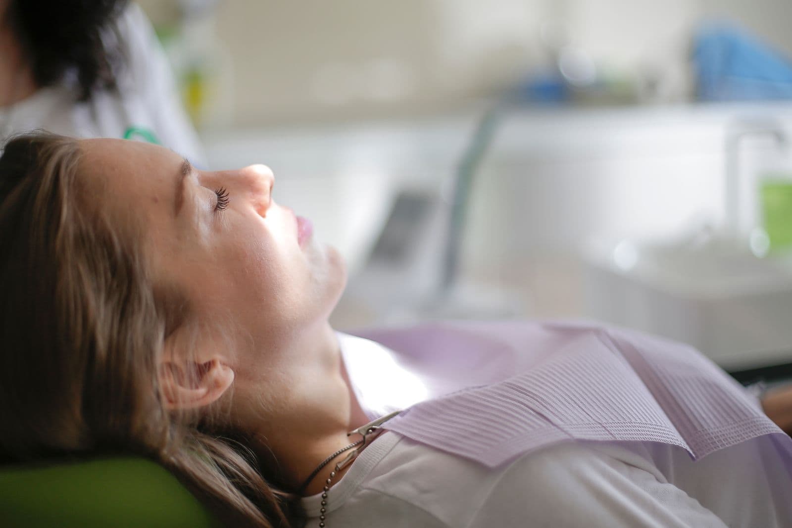 A patient reclined in a dental chair with a dentist leaning in, shot close so the background falls out of focus.